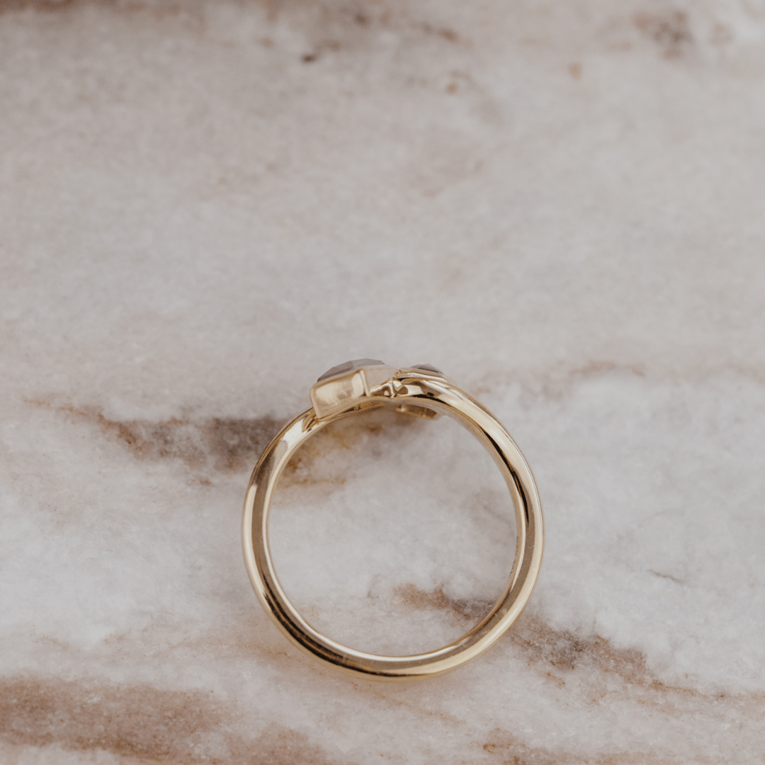 A polished yellow gold ring with rustic diamonds resting on a light beige marble surface.
