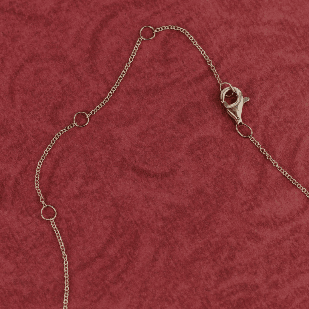14k gold emerald cut, lab grown diamond chain necklace showcased on a textured red surface showing the clasp.