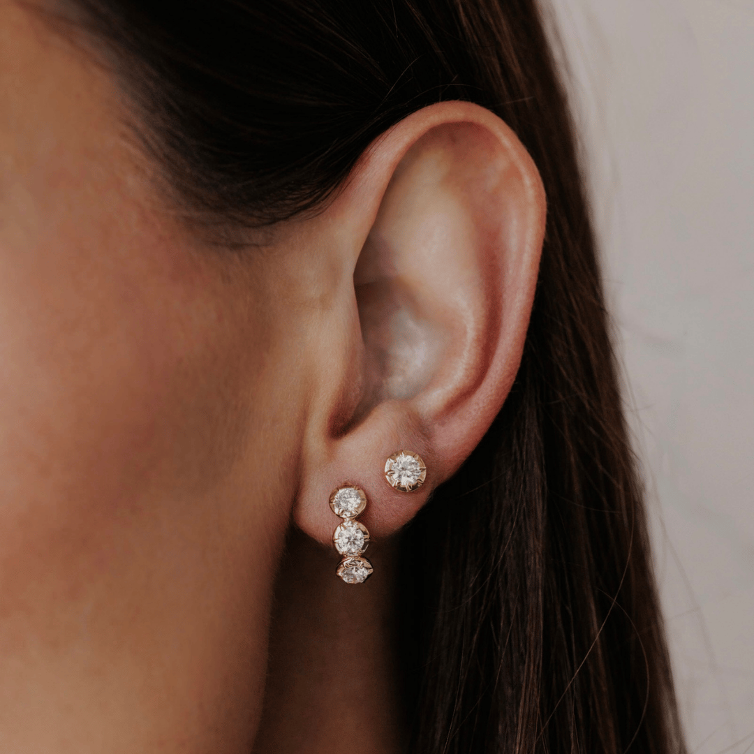 14k gold three round lab grown diamond huggie earrings showcased on the ear of a model.