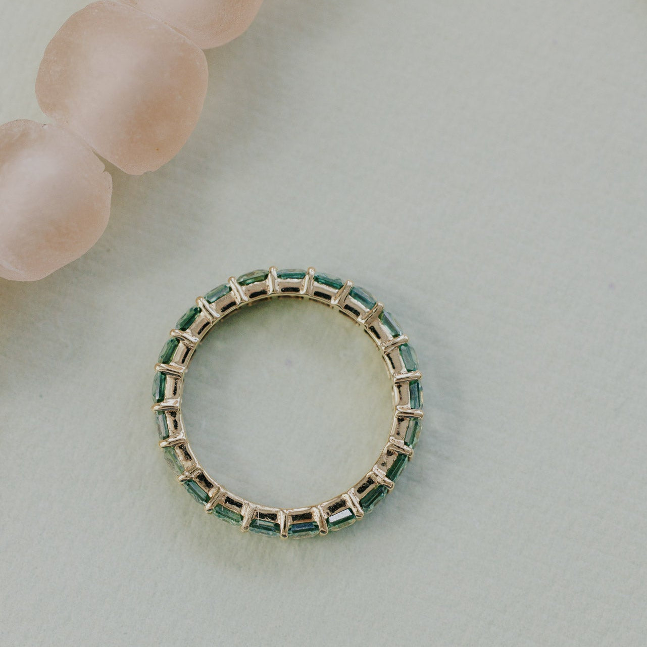 Gold band with green sapphires on a light background.