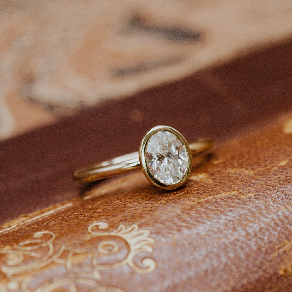 Gold Bailey engagement ring with a oval diamond on an old book.