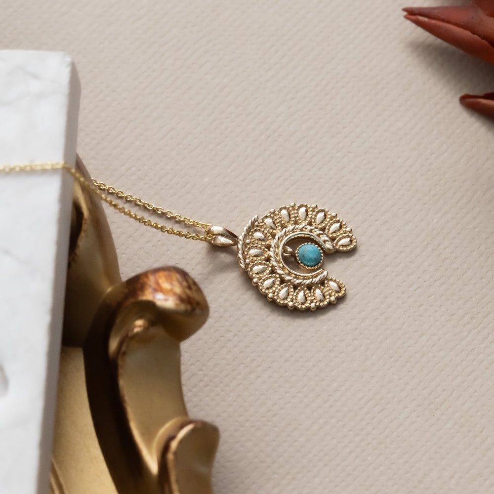 Gold necklace with a turquoise pendant on a beige surface