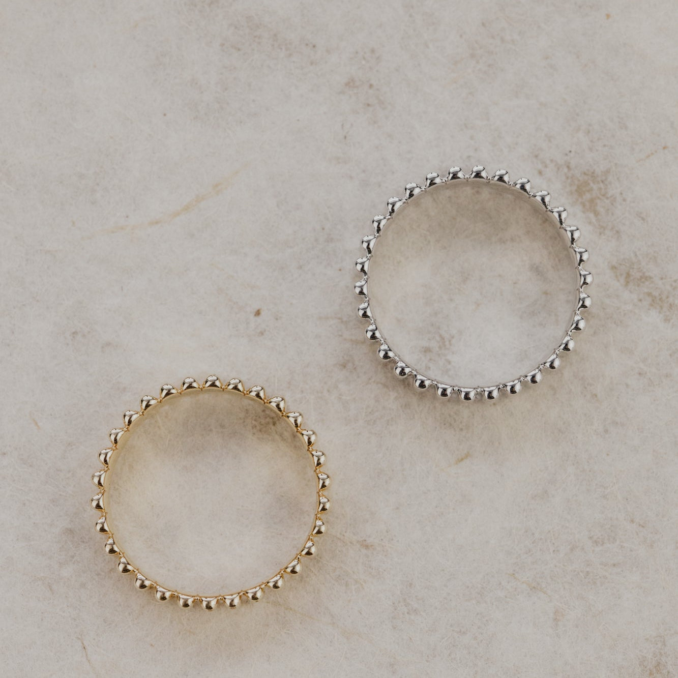 Two Drew ribbed bands in yellow and white gold on a beige marble surface.