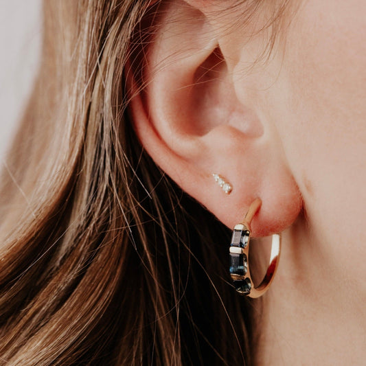 Close-up of an ear wearing a gold hoop earring with a blue topaz gemstone.