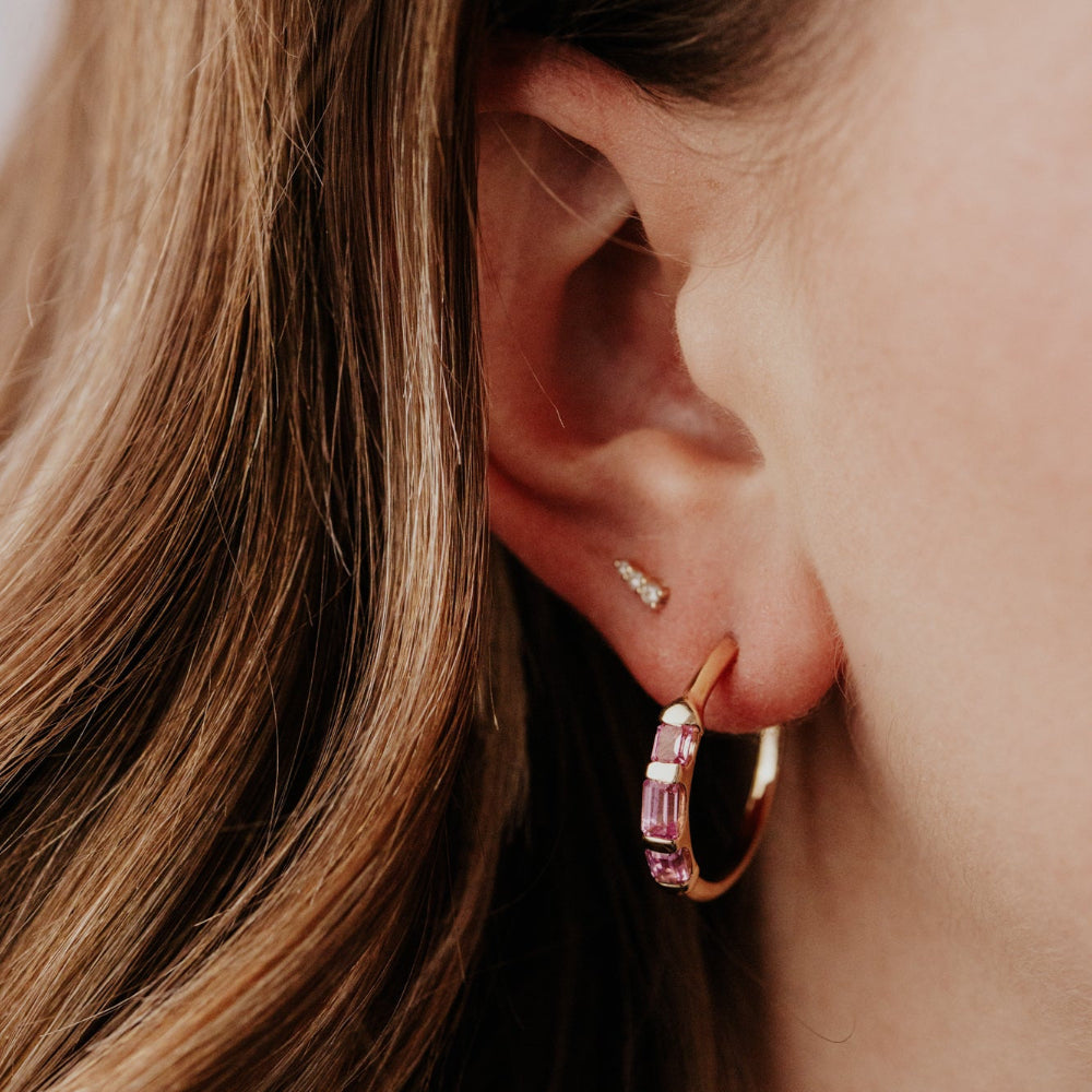 Close-up of an ear wearing a gold hoop earring with pink gemstones.