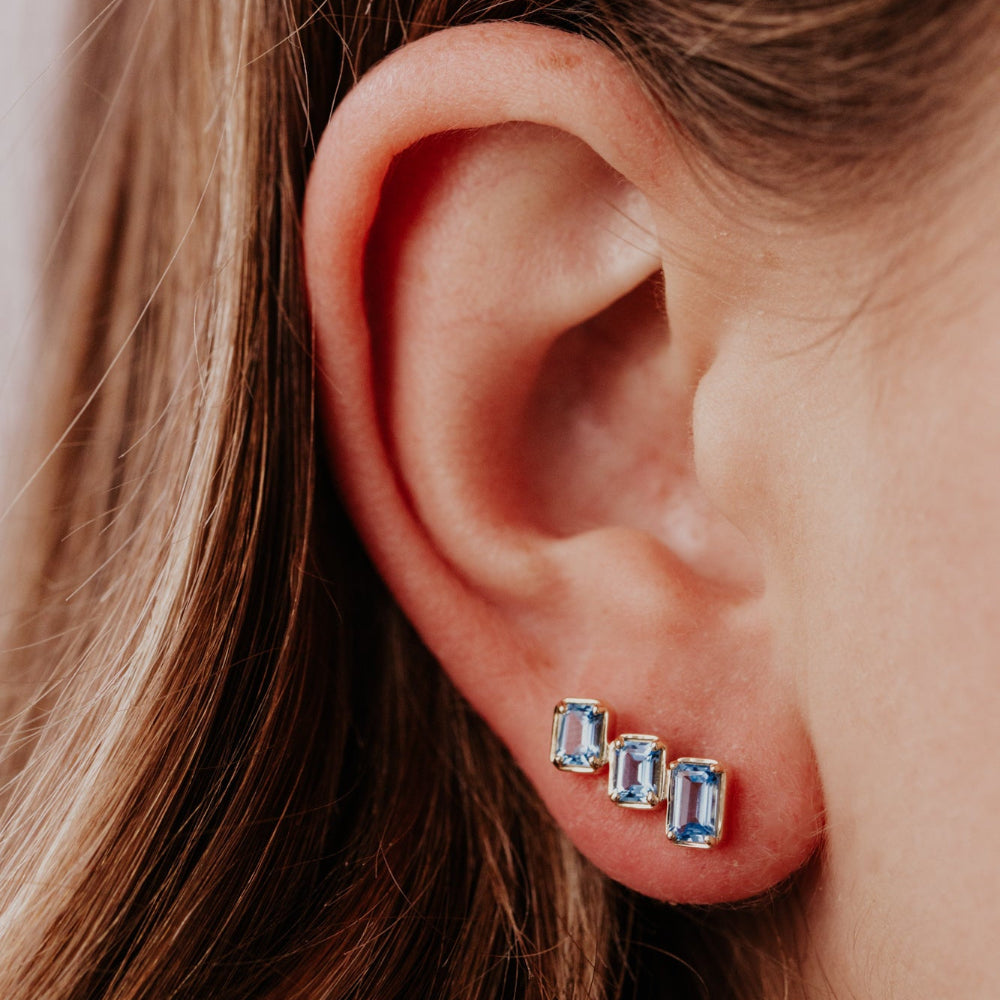 Close-up of an ear wearing three blue gemstone stud earrings.