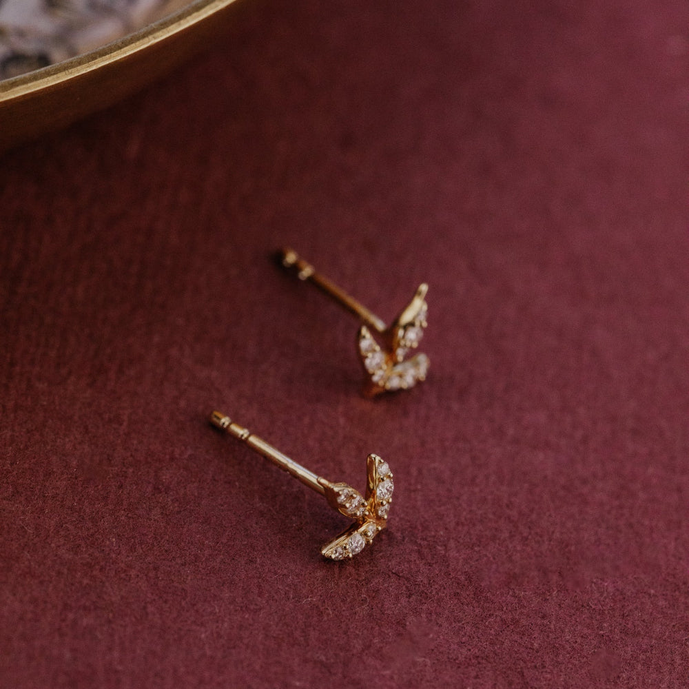 Gold diamond stud earrings with diamond accents on a burgundy surface.