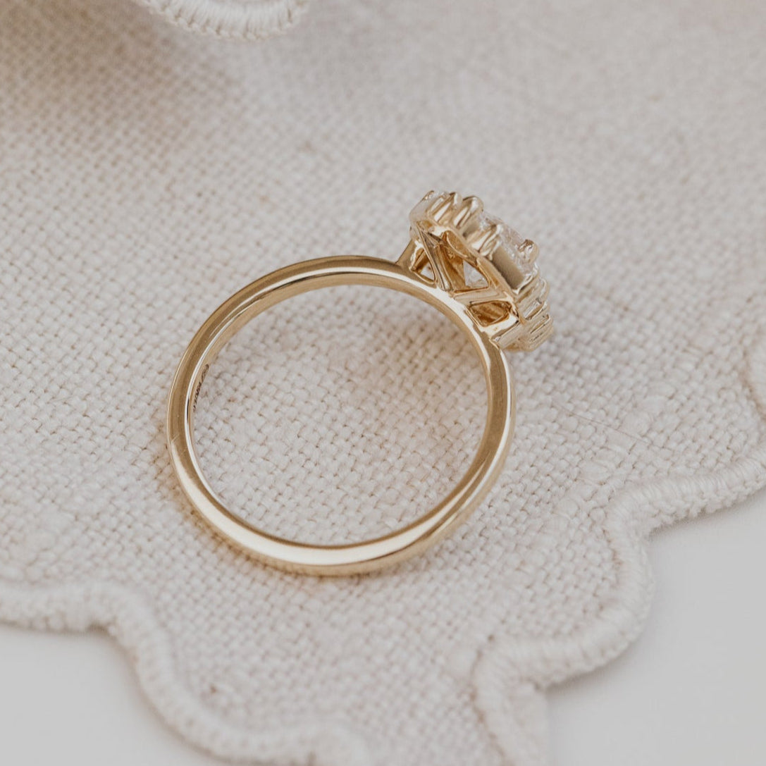 Gold Lori engagement ring with a diamond on a textured beige surface.