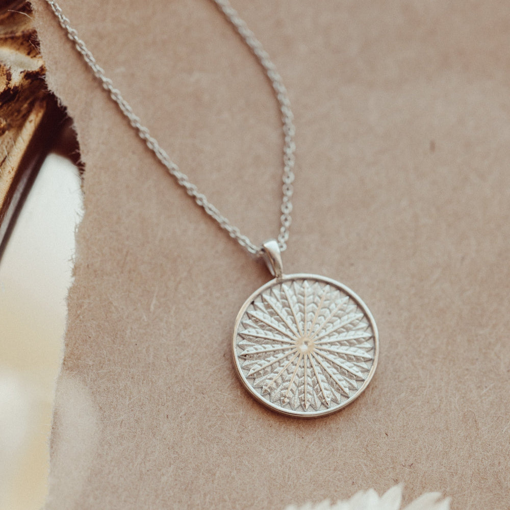 White gold charm necklace with a circular pendant on a beige background
