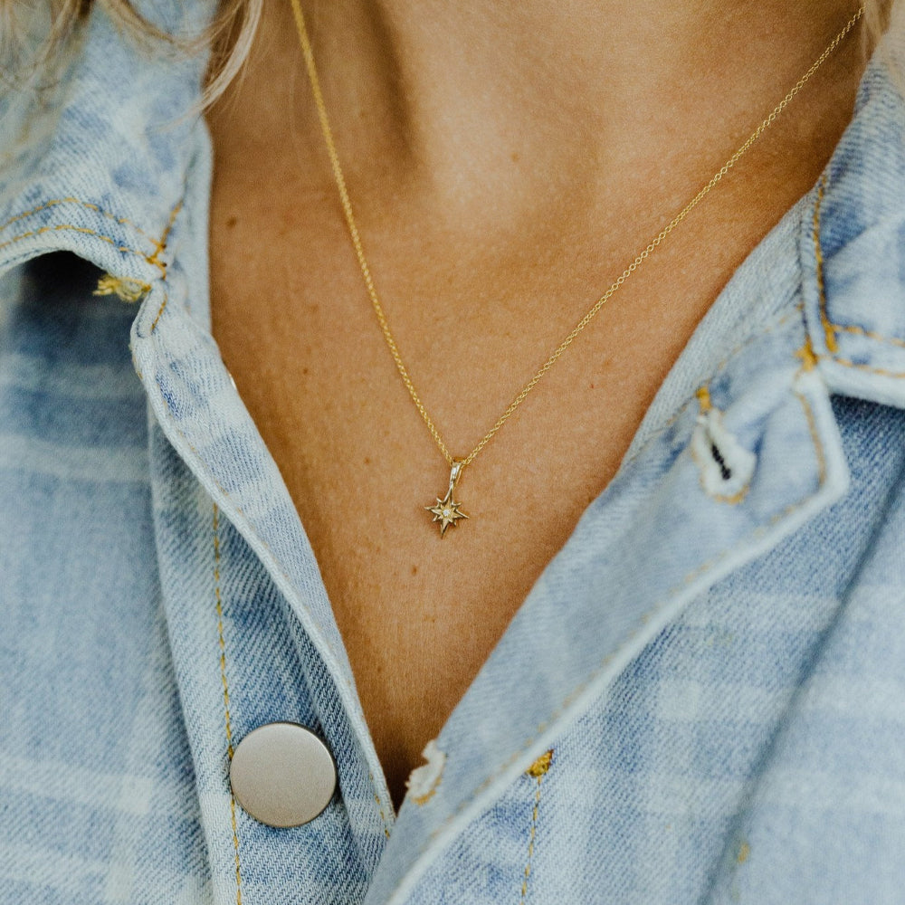 Gold necklace with a star pendant worn by a person in a denim jacket.