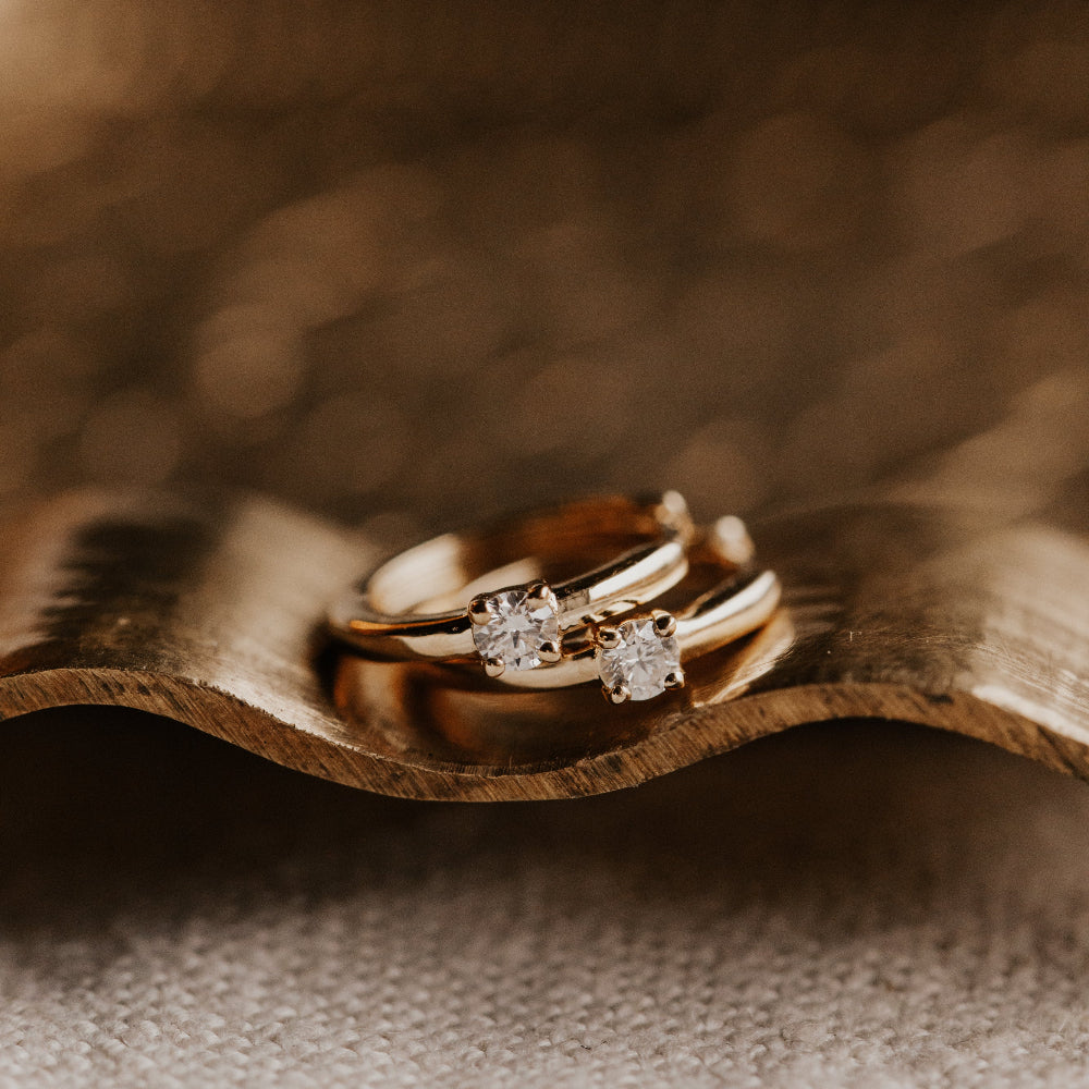 Pair of gold diamond huggie hoop earrings on a wooden surface with a blurred background