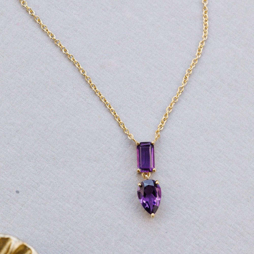 Gold necklace with purple amethyst gemstones on a light gray background
