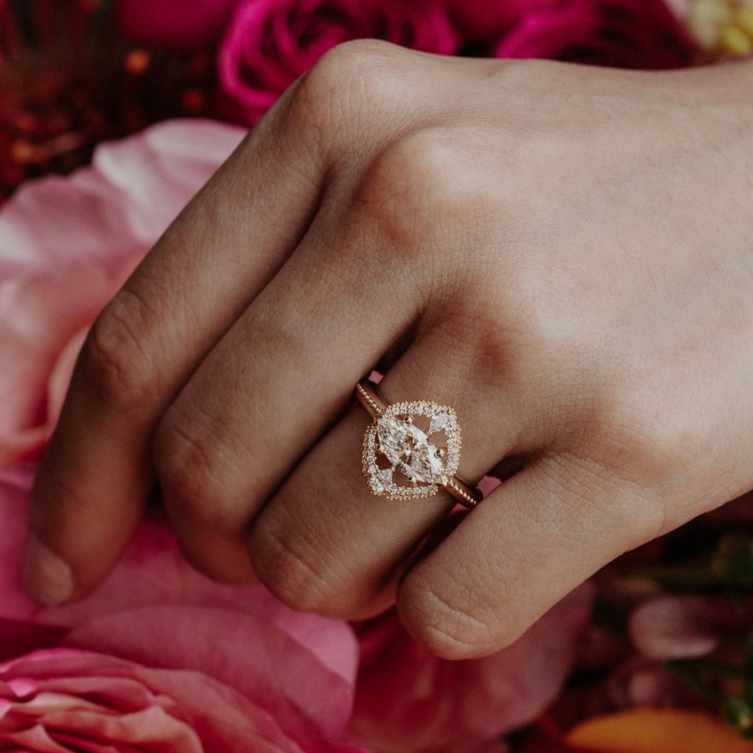 Hand wearing a diamond halo ring with pink roses in the background
