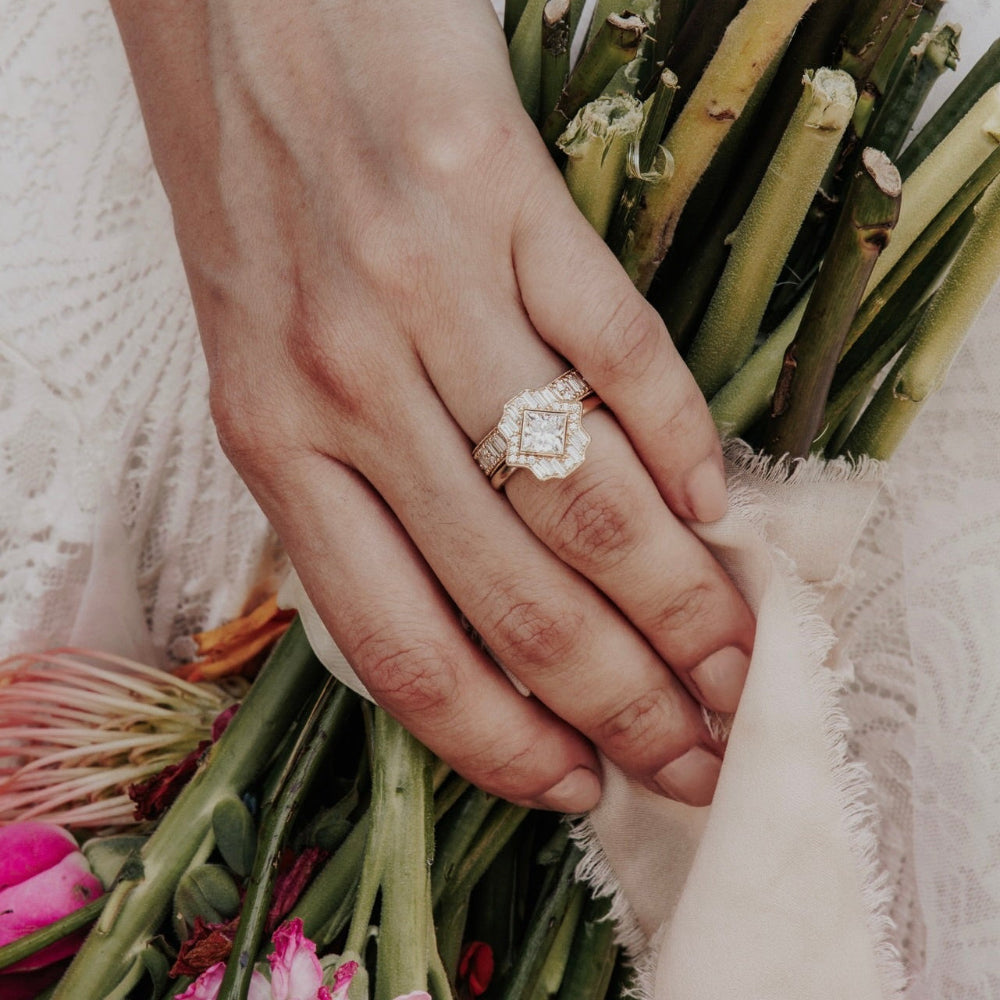 Hand holding a bouquet of flowers with a diamond halo ring on a soft background