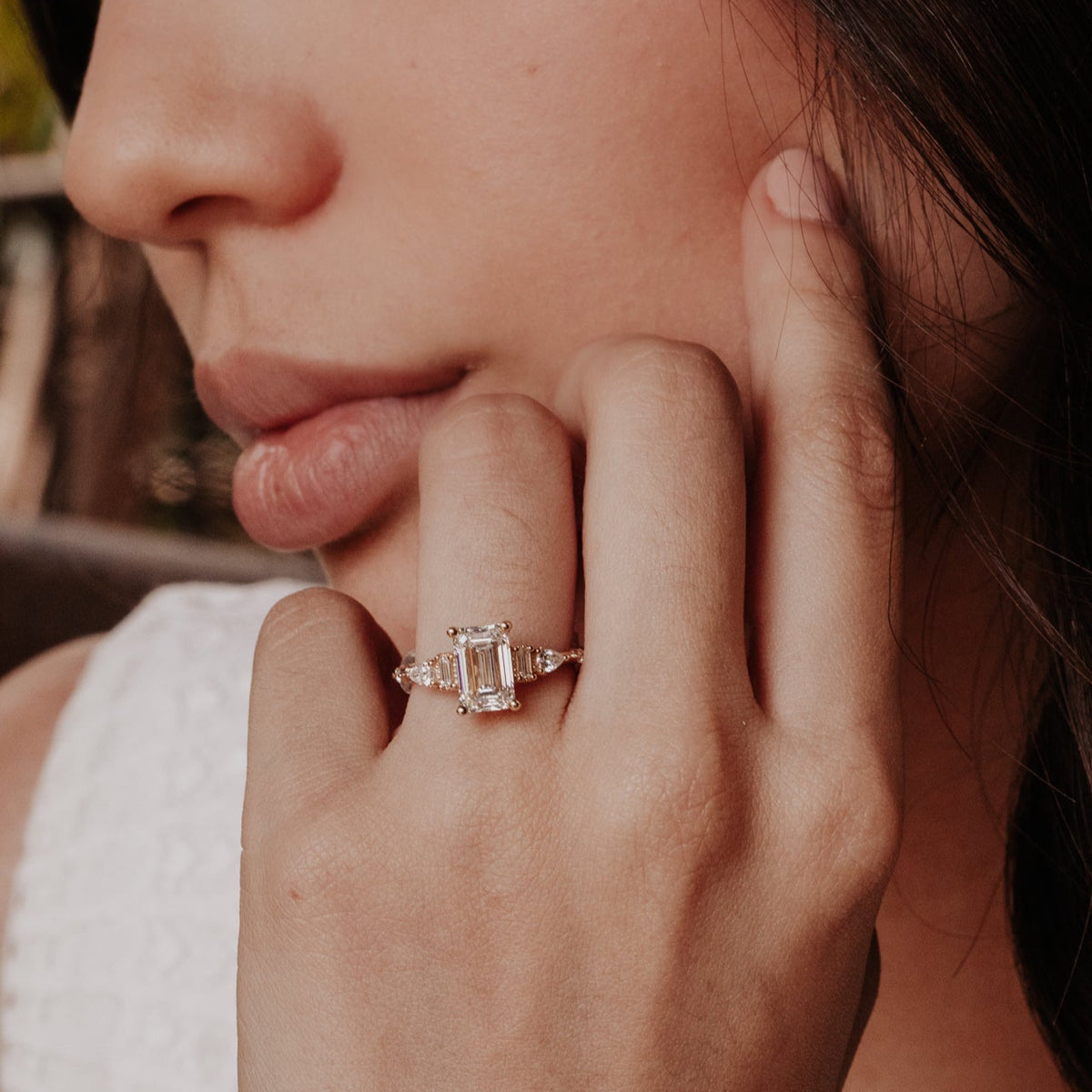 Close-up of a hand wearing a diamond emerald cut ring with a blurred background