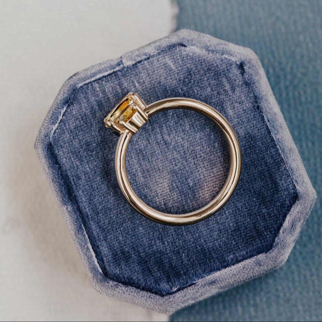 Gold ring  with a Montana sapphirein a hexagonal blue velvet box on a light blue background