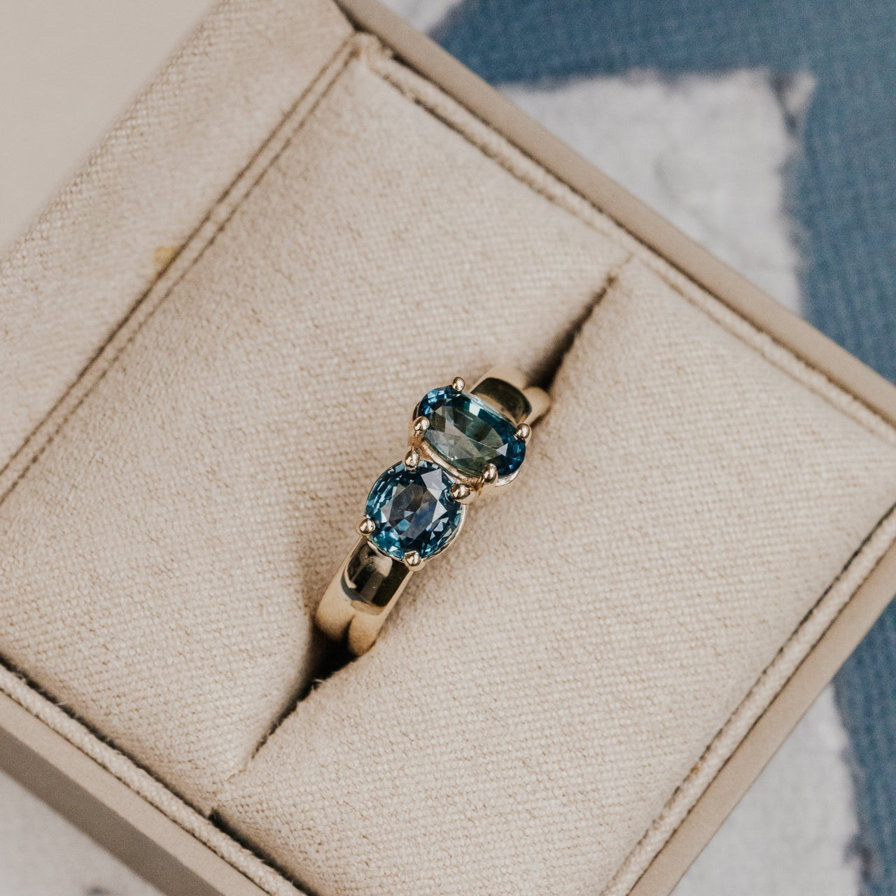 Gold ring with blue Montana sapphire gemstones on a beige jewelry box