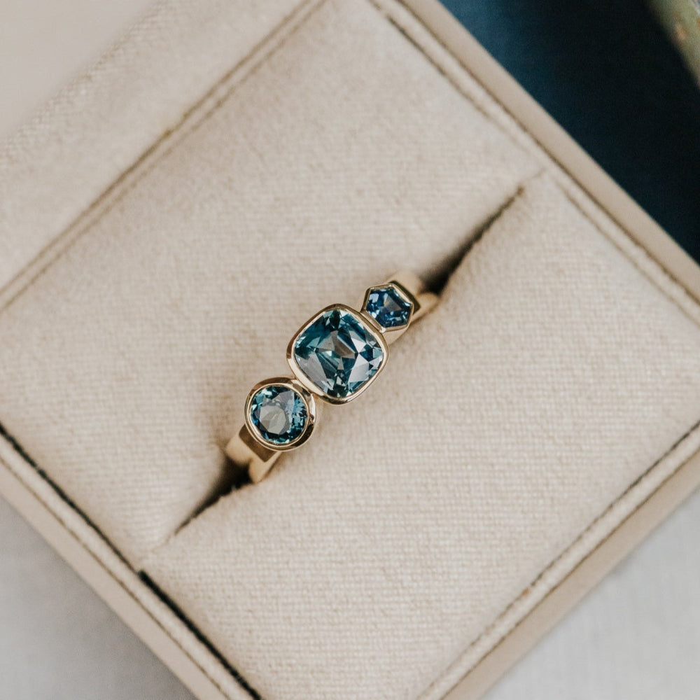Gold ring with cushion blue Australian sapphire gemstones on a beige jewelry box