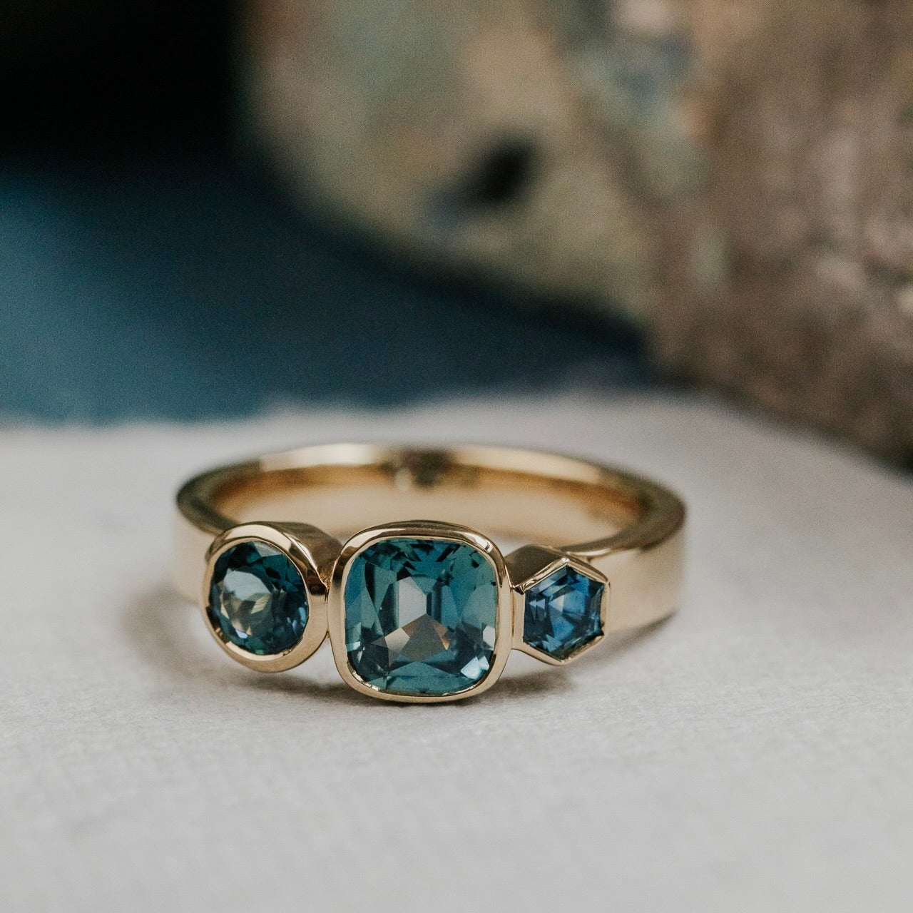 Gold ring with cushion blue Australian sapphire gemstones on a textured surface