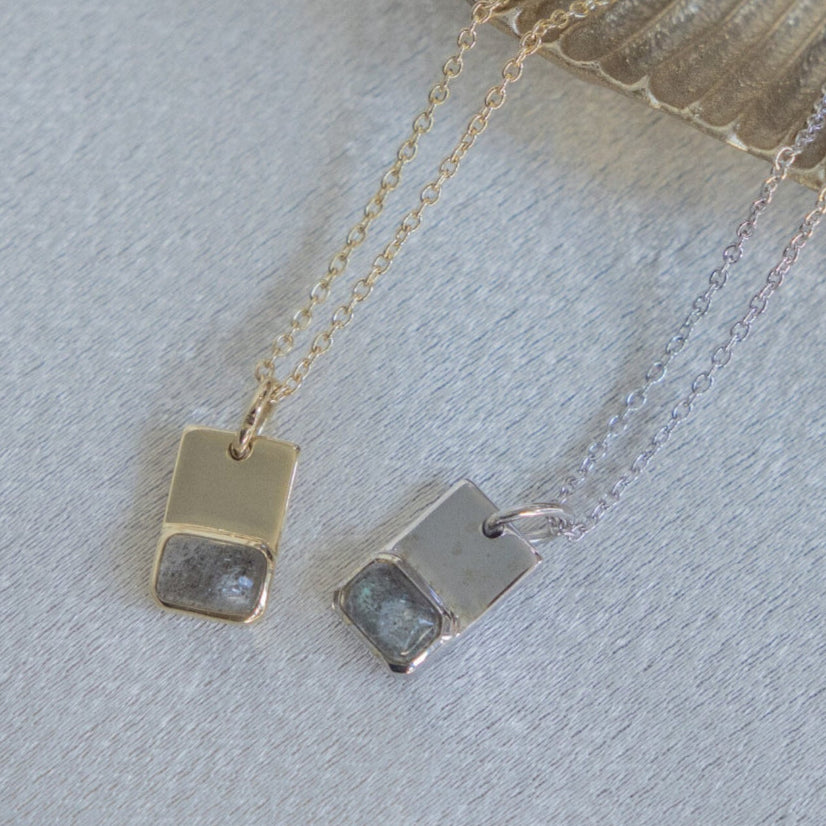 A 14k gold necklace with an emerald cut labradorite pendant in a bezel, accompanied by a gold rectangle accent, on an adjustable length chain.
