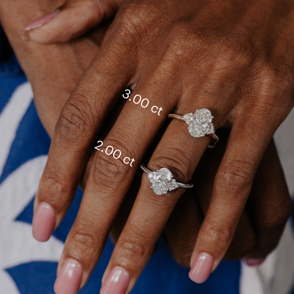 Two diamond rings on a hand with '3.00 ct' and '2.00 ct' labels against a blue and white floral background.