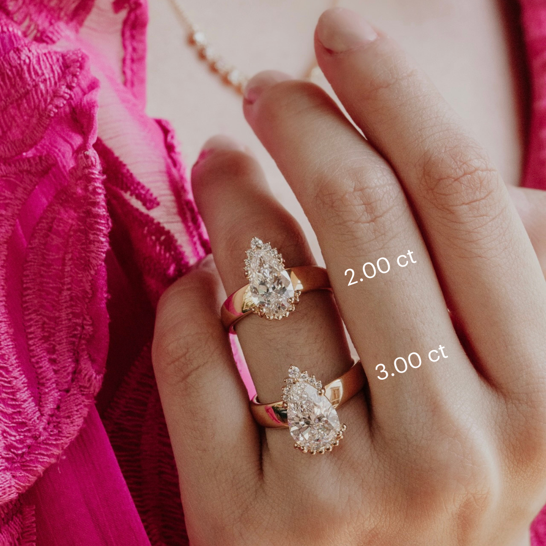 Hand wearing two diamond rings with visible carat weights against a pink fabric background