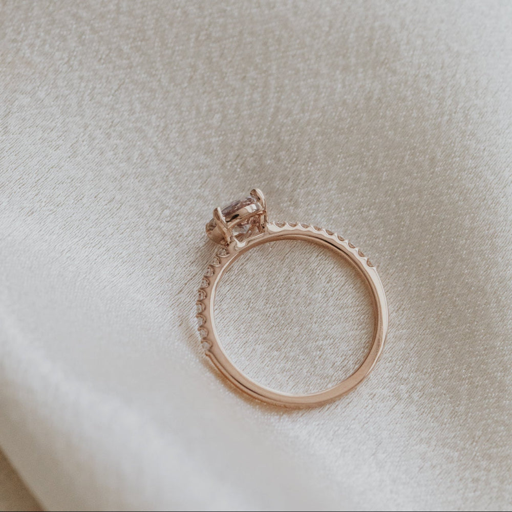Rose gold ring with a light pink Sri Lanka Sapphire and a pave diamond band on a light beige background