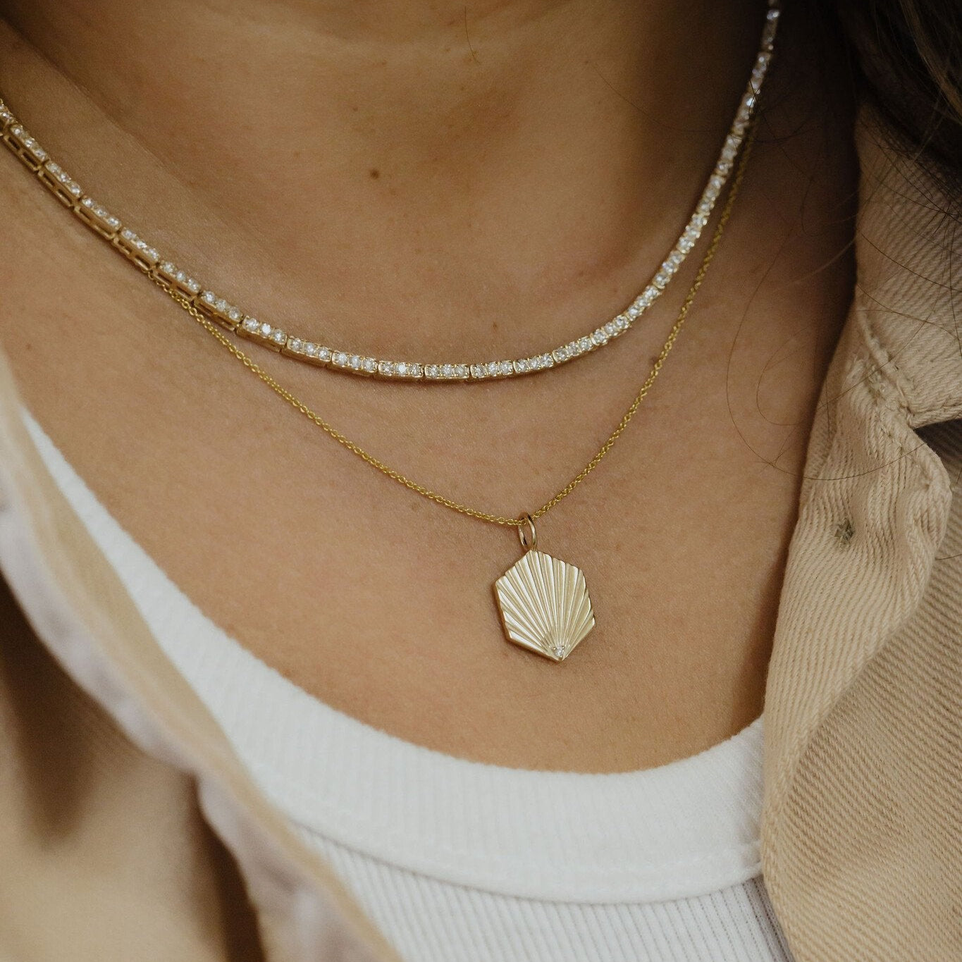 Close-up of a person wearing two gold necklaces with shell pendants.