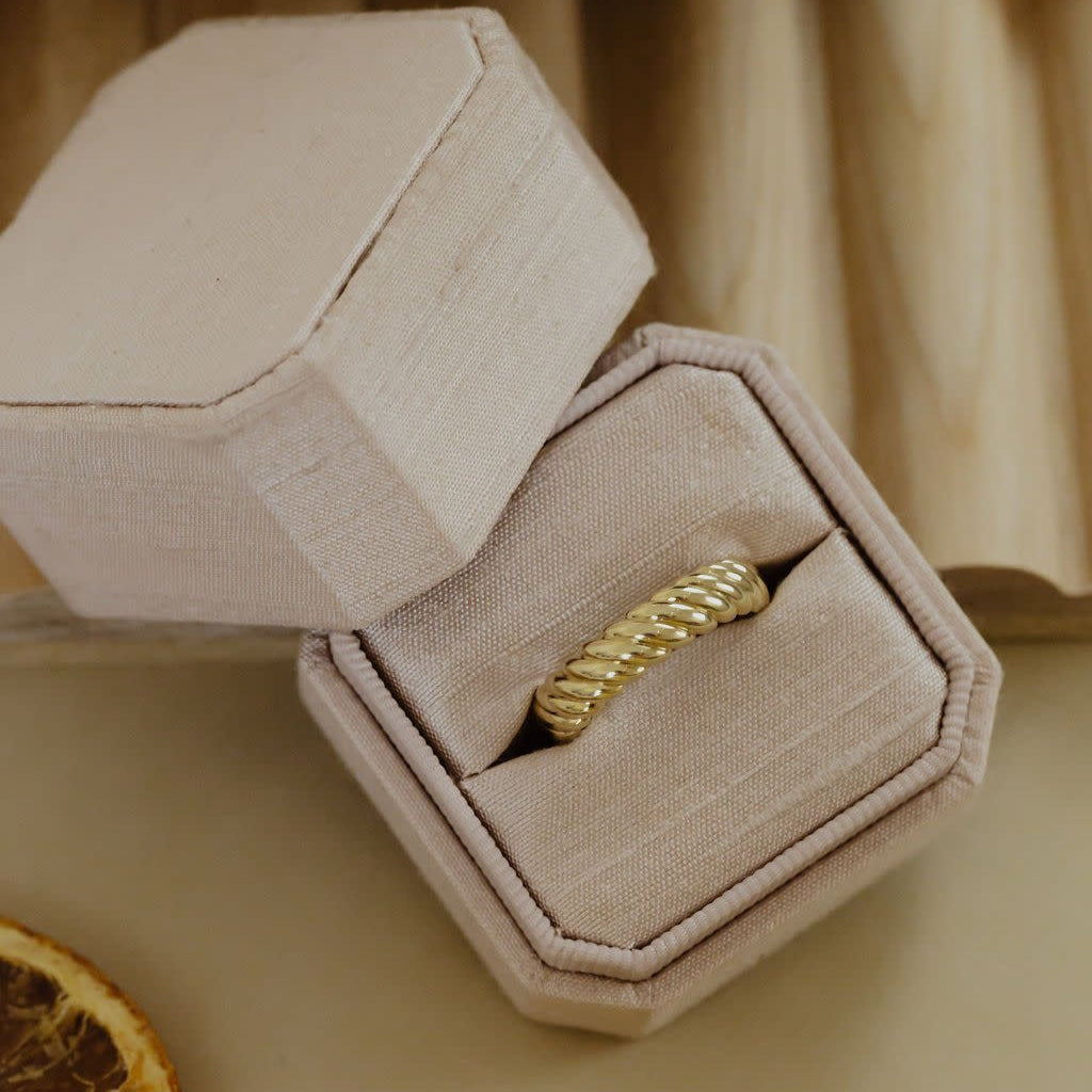 A 14k yellow gold ring with a rope pattern design, displayed in a gray box with a yellow cloth background.