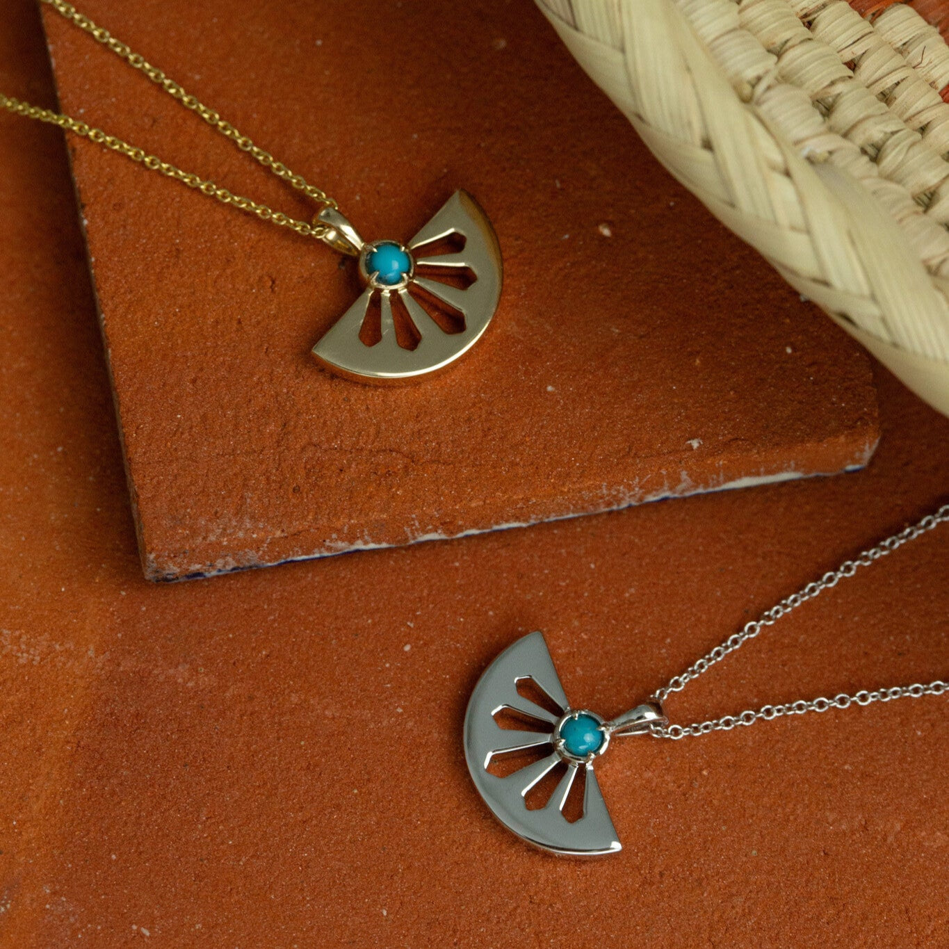 Two gold necklaces with fan-shaped pendants and turquoise stones on a brown surface.