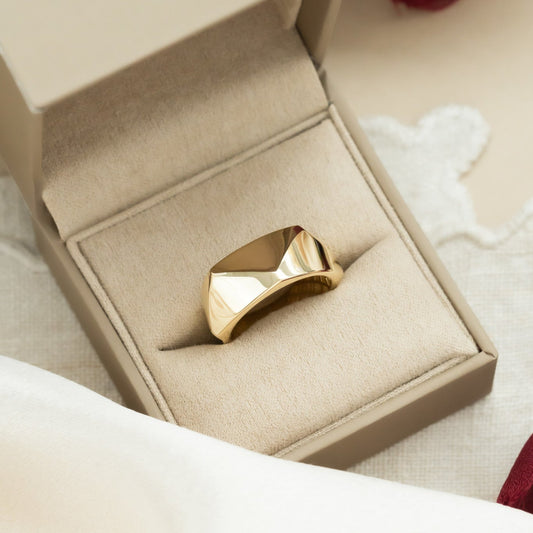 A 14k yellow gold ring with a large geometric texture, displayed in an open box alongside a white silk surface.