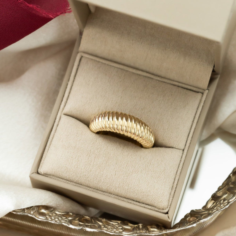 A 14k yellow gold ring with a rope texture on a tapered band, displayed in an open box with a soft fabric lining.