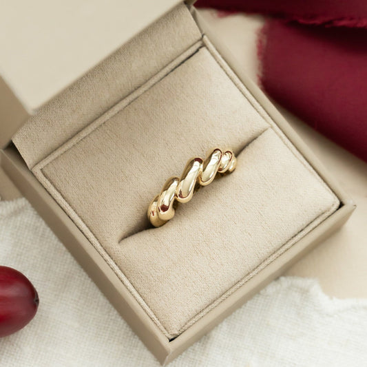 A 14k yellow gold chunky twist ring in a beige setting, presented in a soft-colored box.