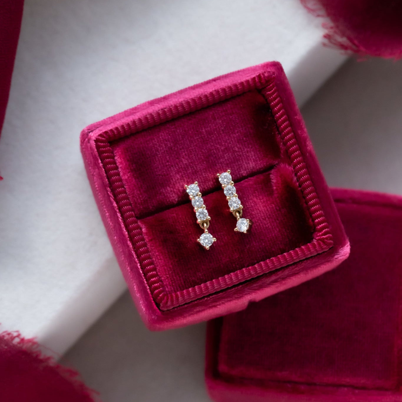 A pair of 14k yellow gold dangle earrings with three diamonds set in a prong, displayed in an open velvet case.