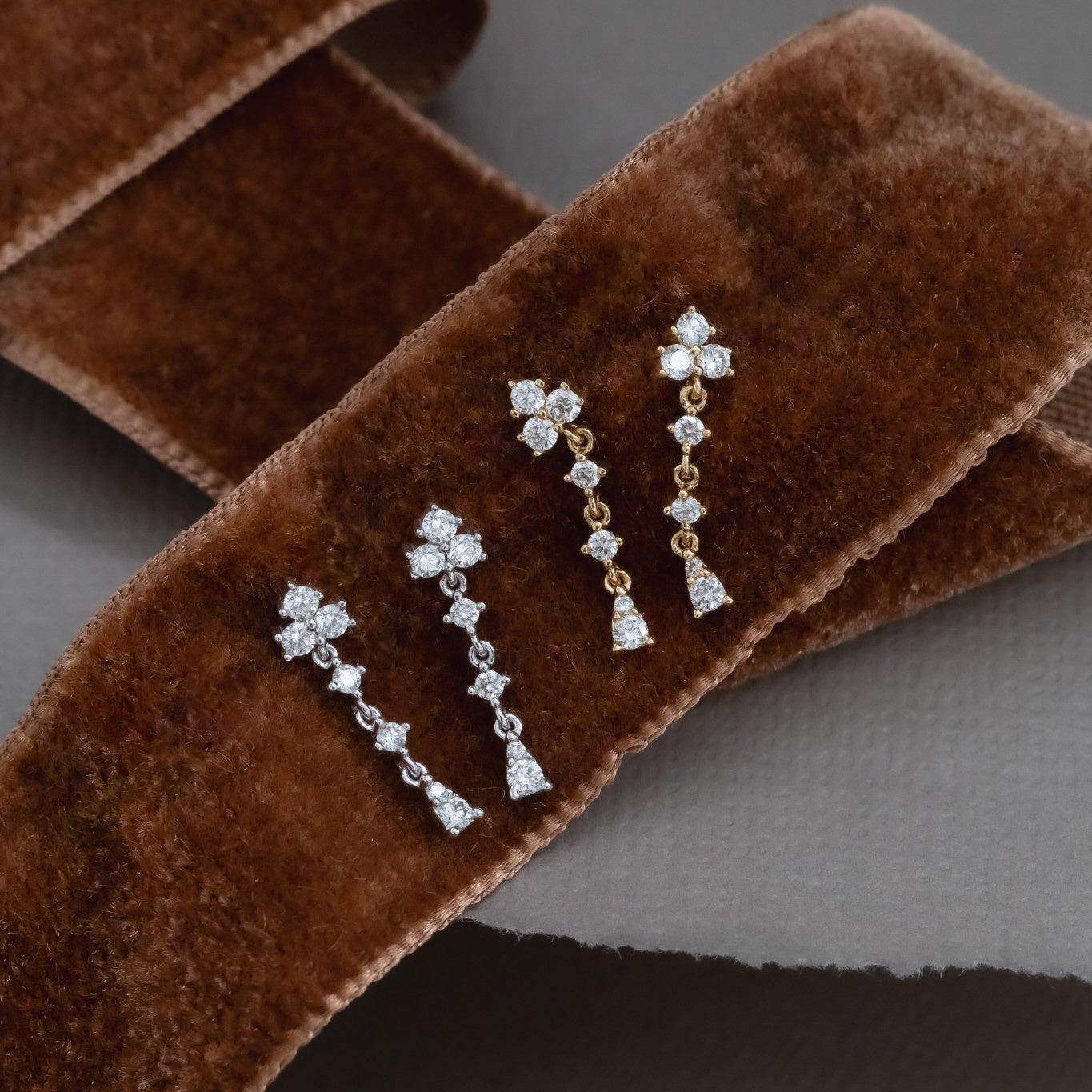 A pair of 14k gold dangle diamond earrings with a cluster design, displayed on a textured surface.