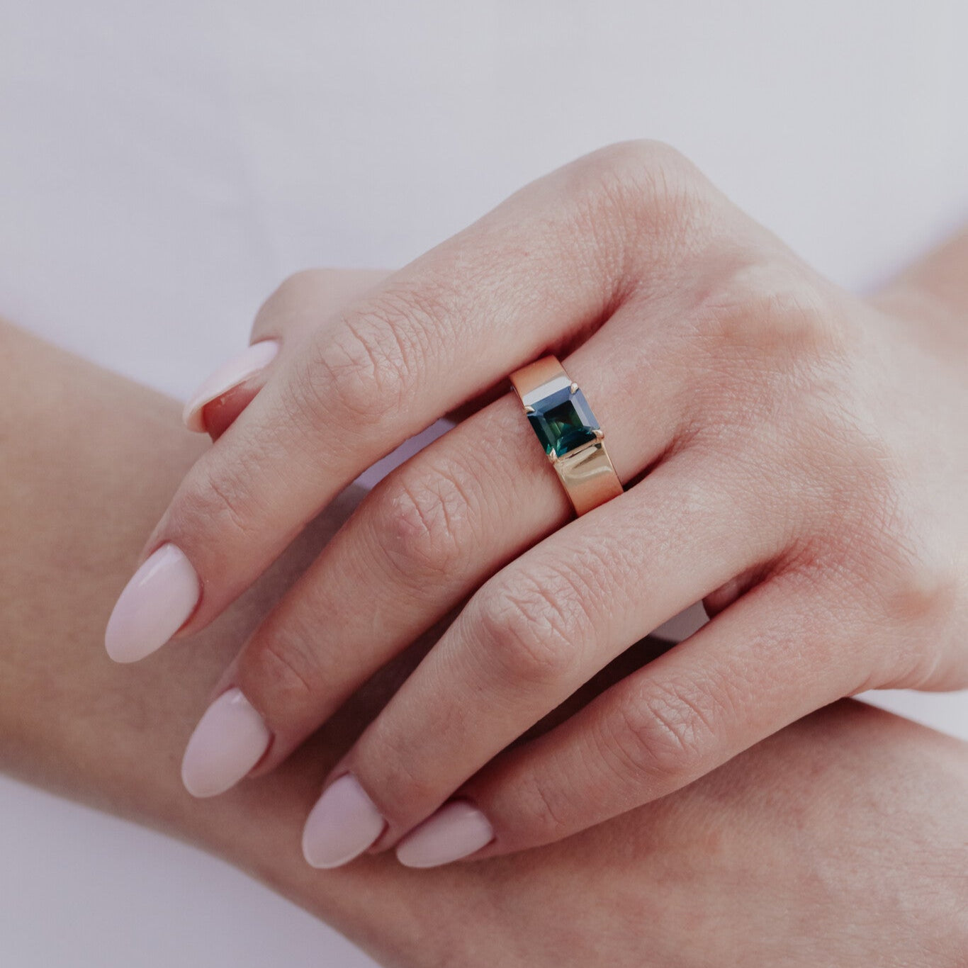 Close-up of a hand wearing a ring with a green sapphire gemstone on a light background
