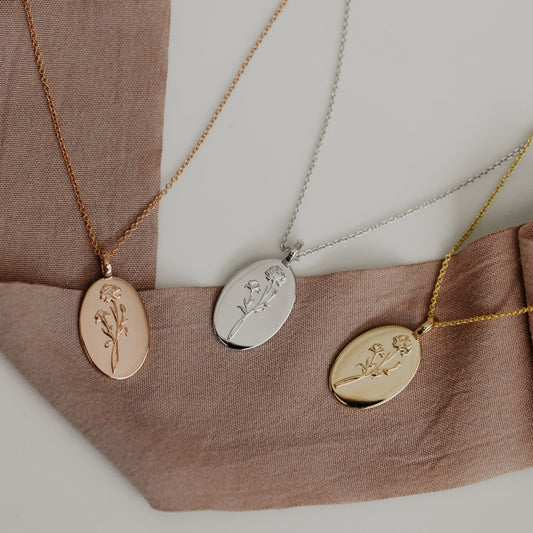 Three wildflower necklaces in rose gold, white gold, and yellow gold colors, displayed on a fabric surface.