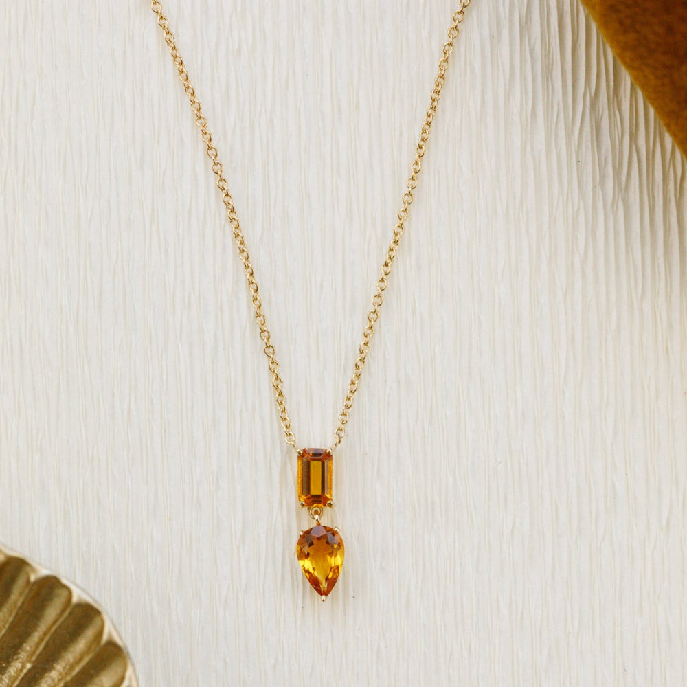 Gold necklace with a  citrine  pendant featuring two orange gemstones on a textured white background.