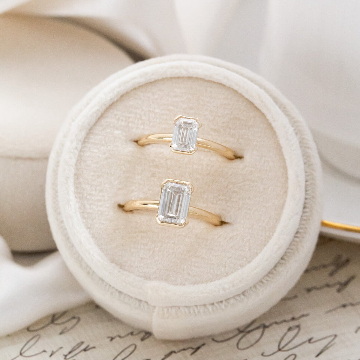 Two Zadie emerald cut diamond engagement ring in different carat weights placed in a white velvet ring box.