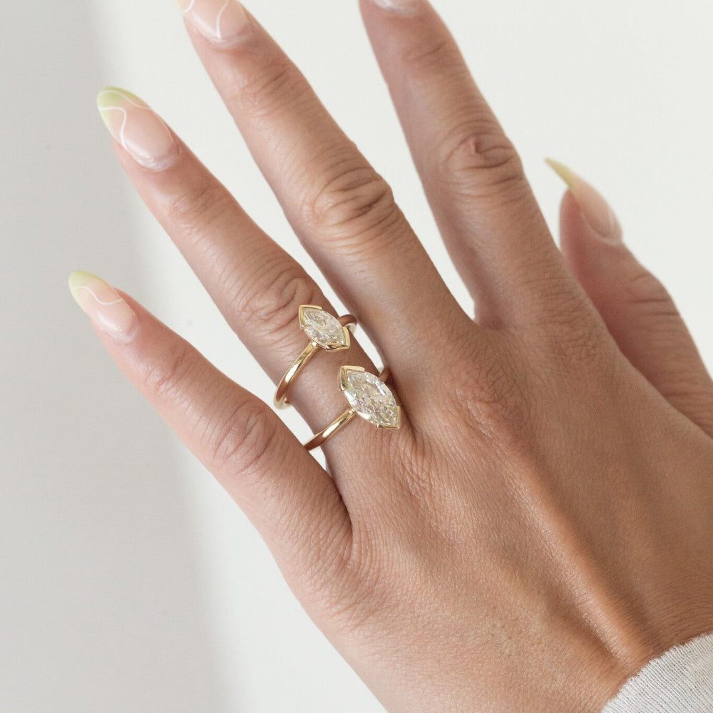 Hand wearing two gold Zadie engagement rings with marquise-shaped diamonds on a light background.