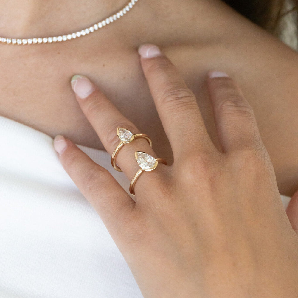 Close-up of a hand wearing two gold Zadie engagement rings with pear-shaped diamond on a white background