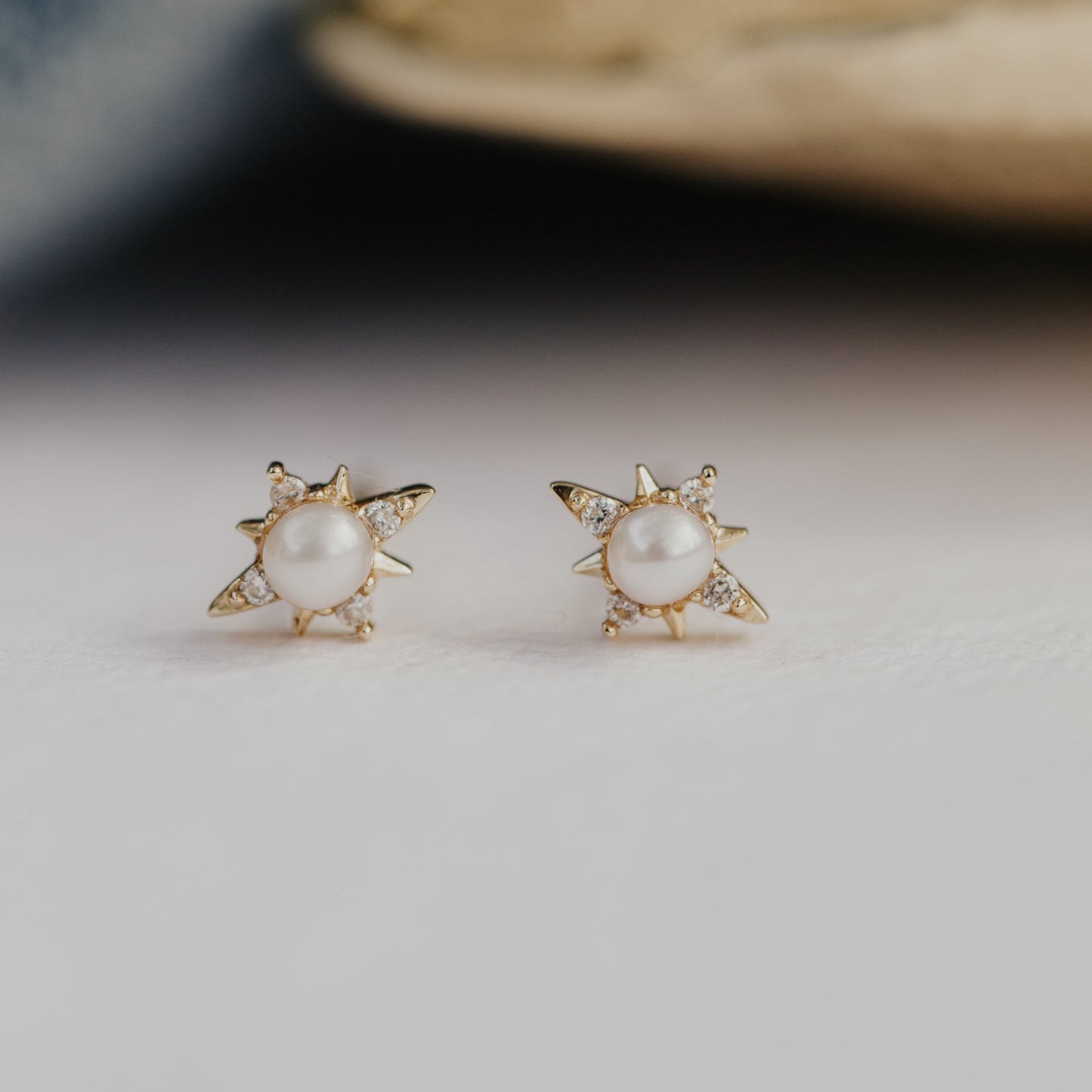 Gold earrings with pearl centers and accent diamond in a star design on a neutral background.