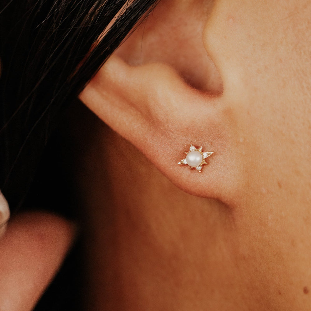 Close-up of an ear wearing a star-shaped earring with a pearl center and diamond accents.
