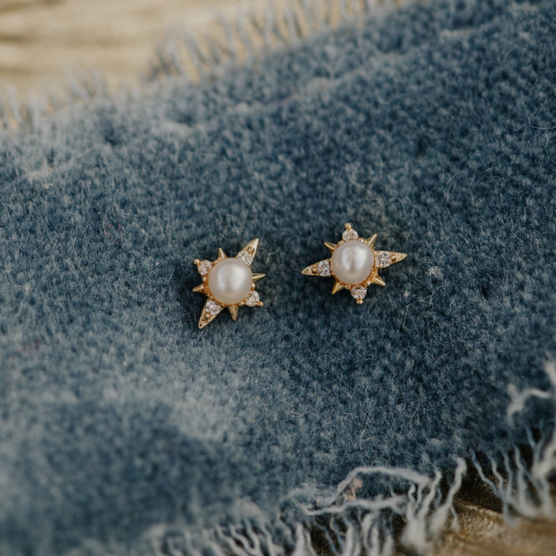 Pair of pearl earrings on a textured denim surface.