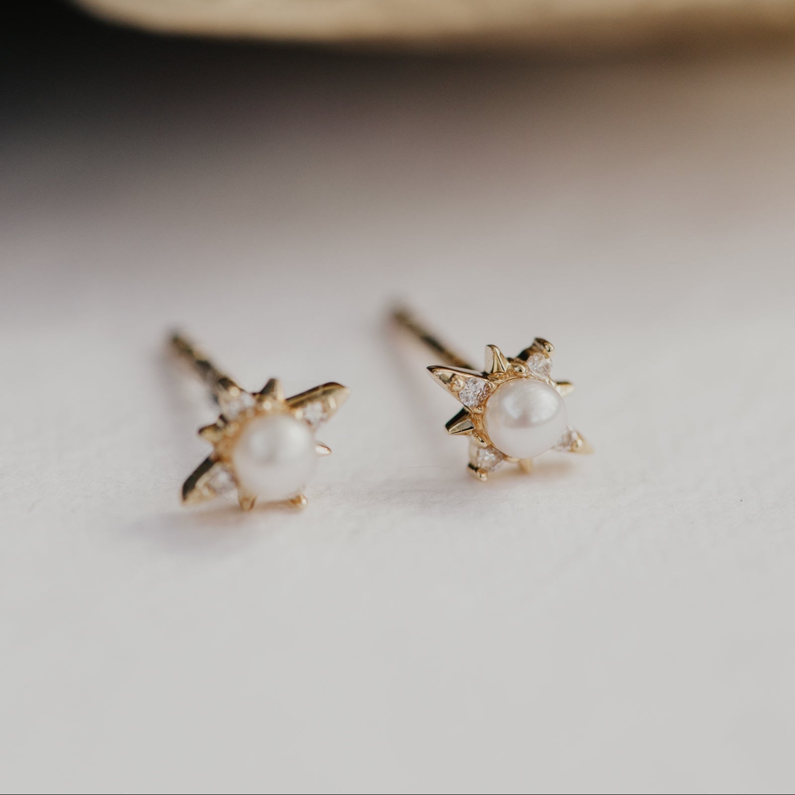 Gold earrings with pear centers on a light surface with a blurred background.