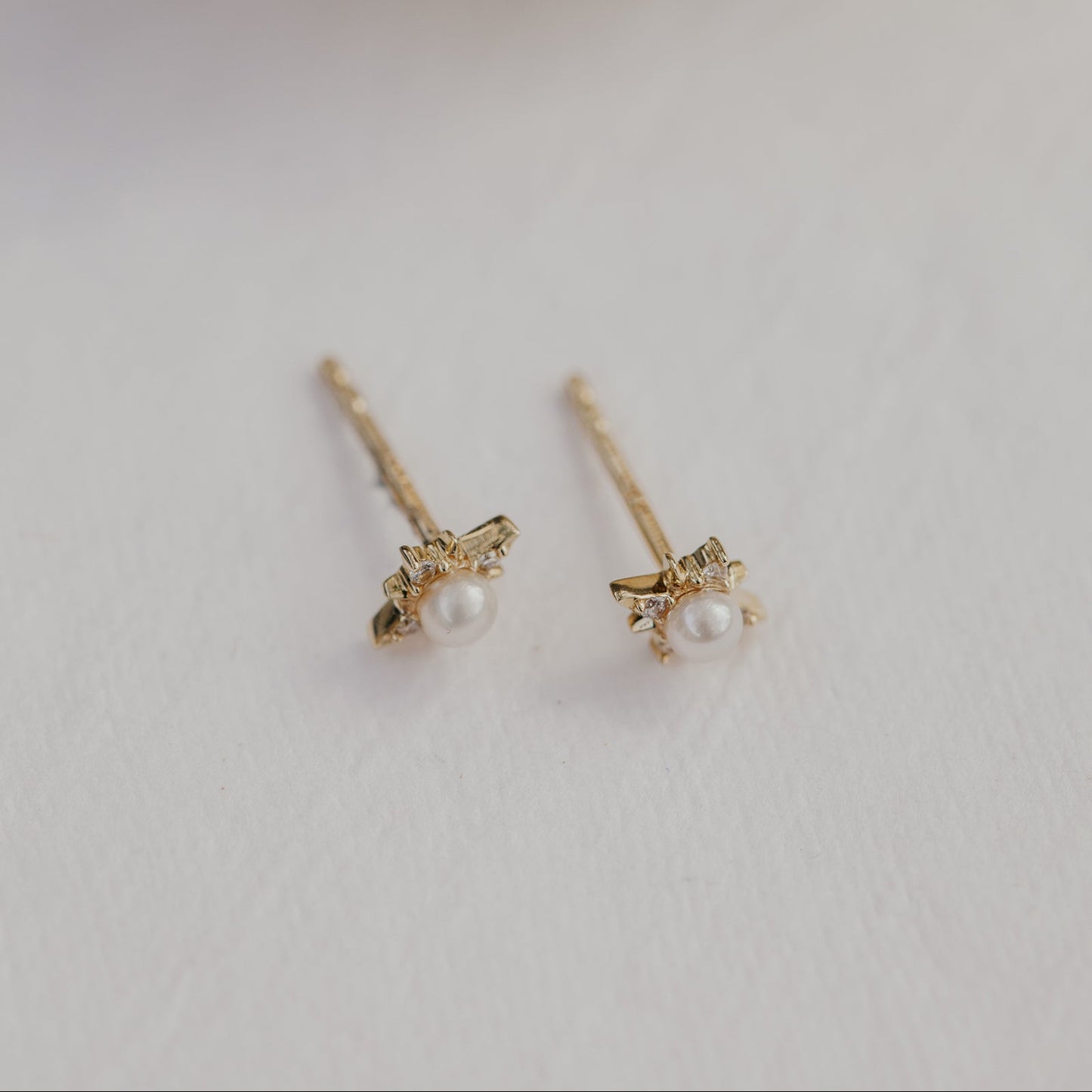 Pair of gold earrings with pearls on a light gray background.