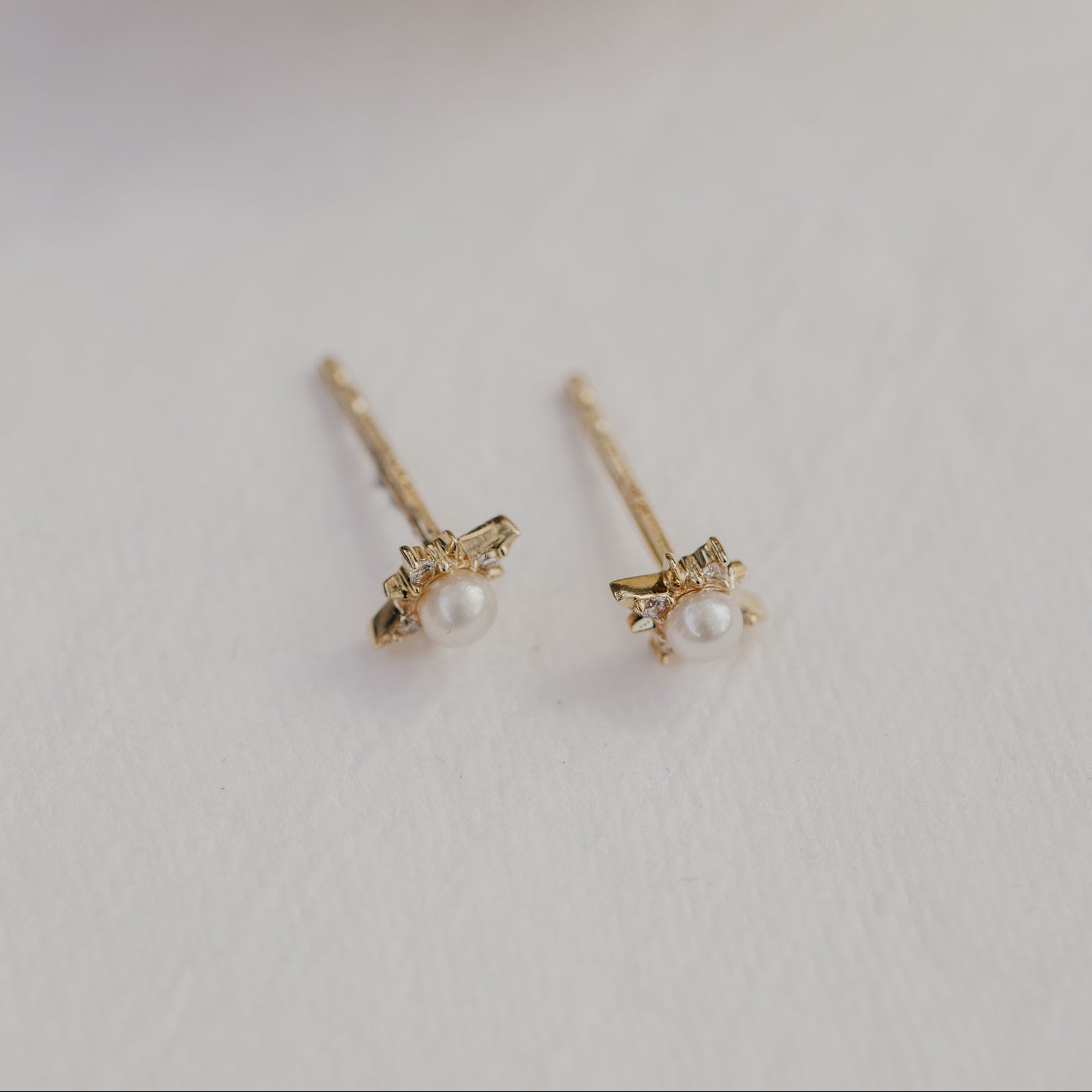 Pair of gold earrings with pearls on a light gray background.