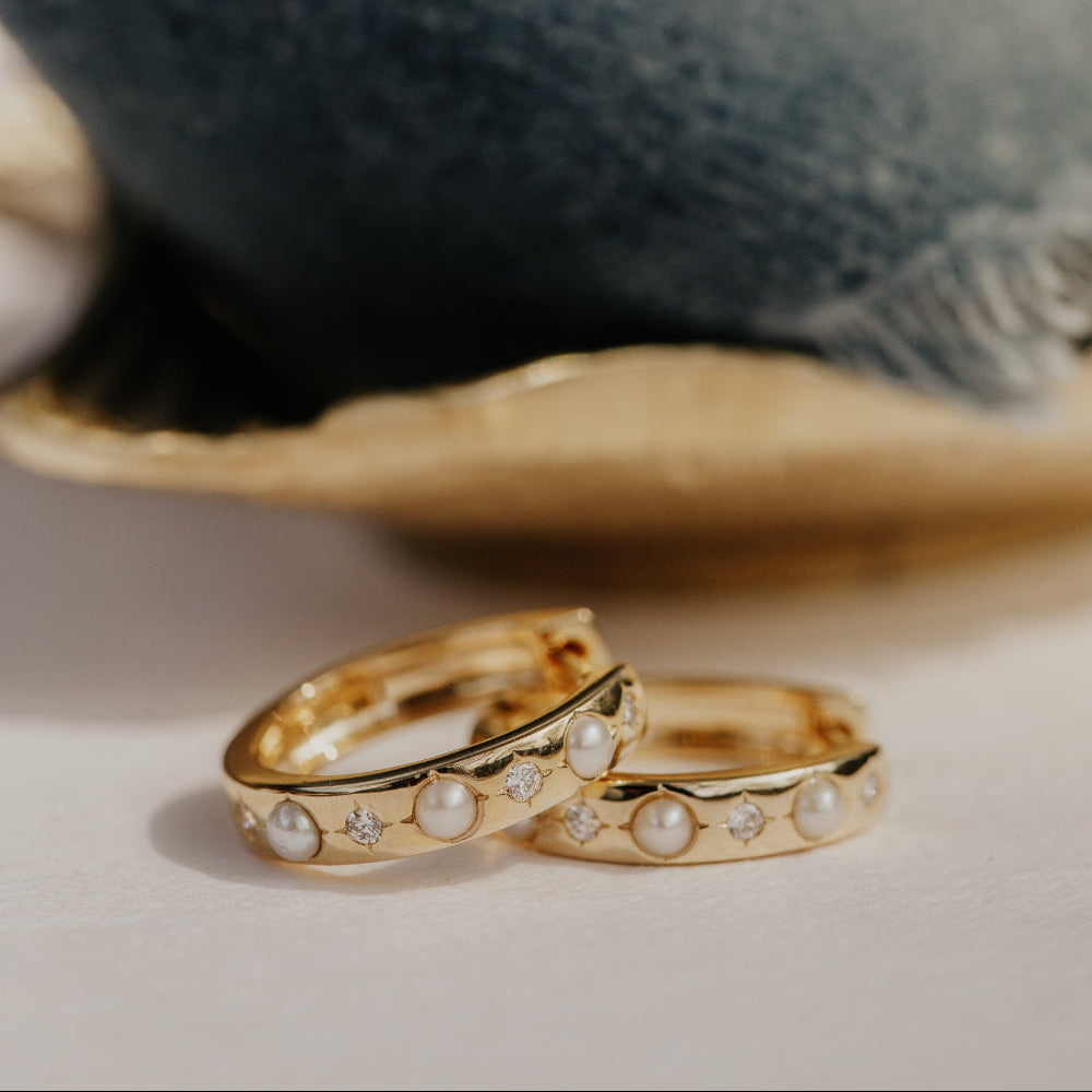 Two gold hoop earrings with pearl accents on a textured surface.