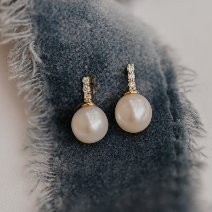 Pearl earrings with gold clasps on a textured blue fabric background.