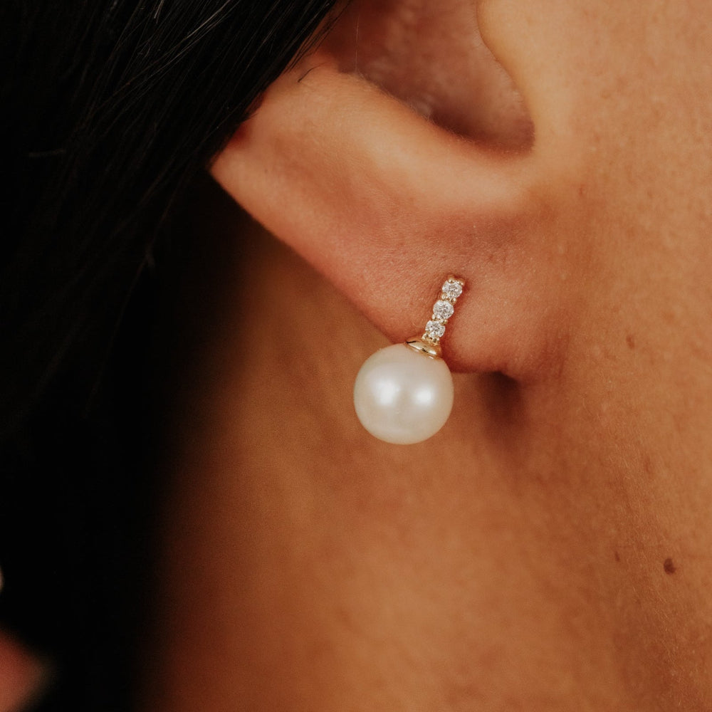 Pearl earring with small diamonds worn by a person.